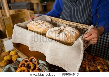 Mid section of staff holding wicker basket of breads at counter in bakery shop