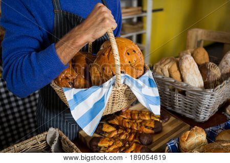 Mid section of staff holding wicker basket of breads at counter in bakery shop