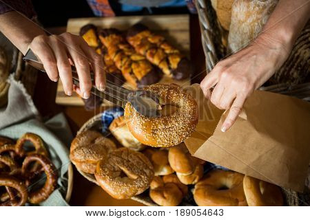 Mid section of staff packing doughnut in paper bag at counter in bakery shop