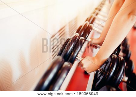 Sports equipment dumbbell rests in a row, girl takes a dumbbell in the gym. hands close-up. hign contrast and monochrome color tone