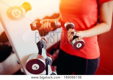 Sports equipment dumbbell rests in a row, girl takes a dumbbell in the gym. hands close-up. hign contrast and monochrome color tone