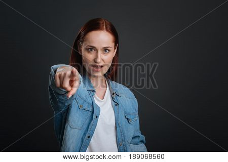 I want you to do that. Graceful inspiring charismatic girl pointing her finger at someone while being very expressive and standing isolated on grey background