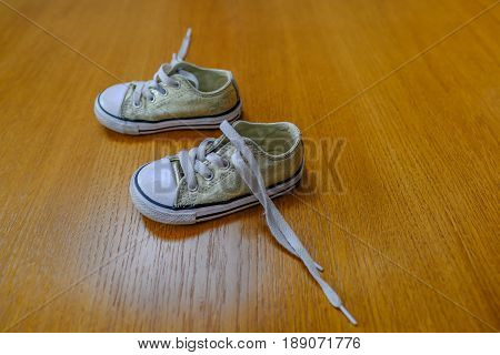 Small child's canvas shoes on an oak floor with trailling laces.
