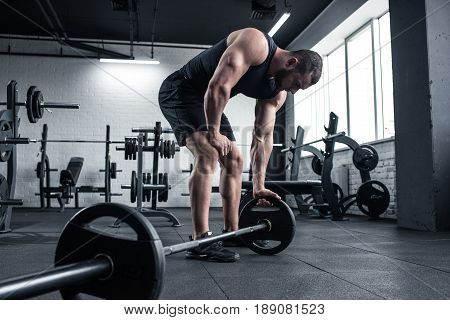 Young Adult Exhausted Bodybuilder Holding Barbell At Gym