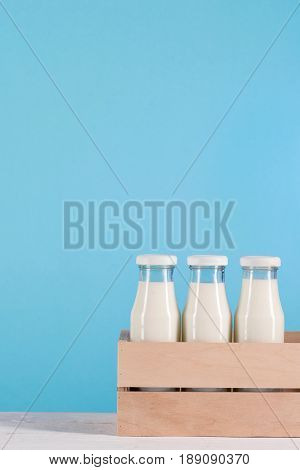 Glass Bottles With Milk In Wooden Box On Tabletop At Blue Background