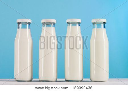 Row Of Glass Bottles With Milk On Tabletop At Blue Background