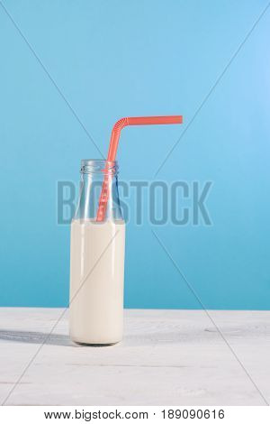 Glass Bottle Of Milk With Straw On Table At Blue Background