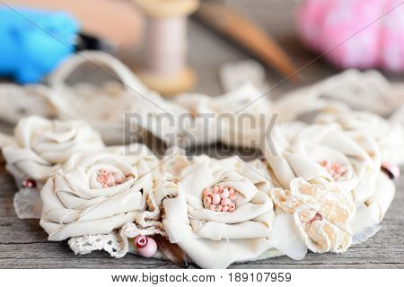 Mixed materials flower necklace, glue hot gun, scissors, thread, needle, felt on vintage wooden table. Summer fashion fabric jewelry for women and girls. Idea of recycling fabric into elegant necklace