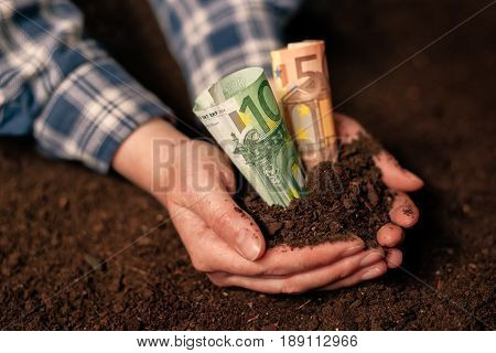 Hands with fertile soil and euro money banknotes female farmer handful of cultivated land that makes profit and steady income from sustainable agricultural activity like organic growth of crops