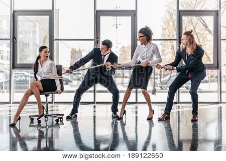 Asian Businesswoman Bound With Rope On Chair And Multicultural Business Team Pulling Her, Team Spiri