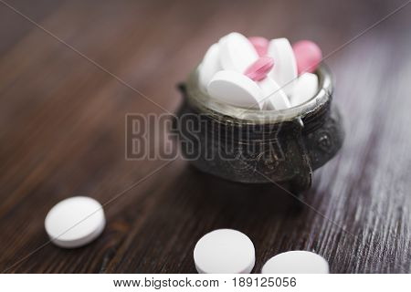 Large white round and small bright pink tablets in a vintage carved pial and several pills next to a dark brown wooden background
