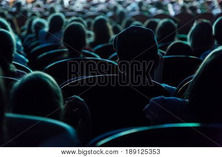 People, children, adults, parents in the theater watching the performance. People in the auditorium looking at the stage. Shooting from the back