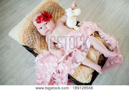 Newborn baby with a red bow on his head lies in a basket with a white knitted toy on a wooden background