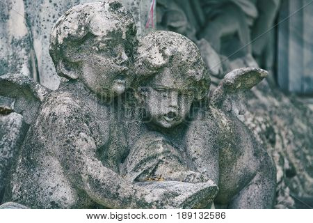 Little angels sculptures on a tomb at a graveyard. Toned image.