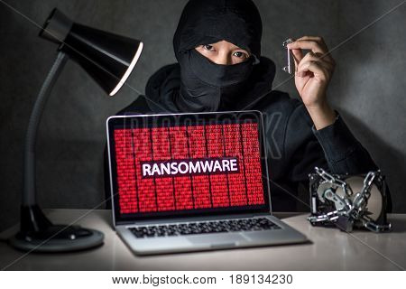 Hacker holding the key with laptop computer screen showing ransomware attacking alert in red digital binary background with hard disk drive lock. Cyber attack concept