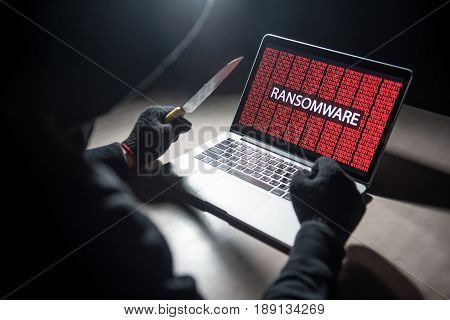 Male hacker threading computer laptop with knife showing on screen with ransomware warning internet security system concept