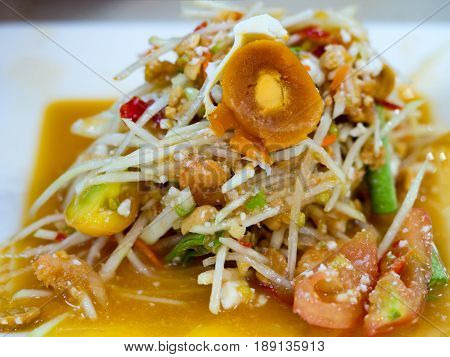 Green papaya salad or Som tum with preserved egg. Popular Thai local food. Spicy salad from shredded unripe papaya sliced tomatoes raw yardlong beans peanuts dried mini shrimp and fresh garlic.