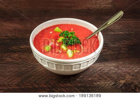 Photo of gazpacho, traditional Spanish soup, garnished with jamon, tomato and onion slices, on a dark rustic background with place for text