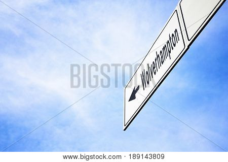 White signboard with an arrow pointing left towards Wolverhampton England United Kingdom against a hazy blue sky in a concept of travel navigation and direction. Path included for the signboard