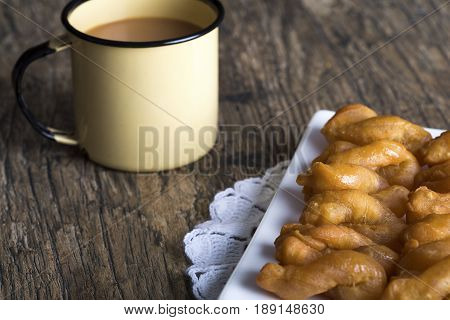 Metal mug full of coffee and a plate of koeksisters on brown wood table