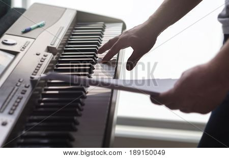 One single finger pressing key on piano. Man looking at paper notes and training a new song or melody from the sheet music. Pianist composing new work or creative producer working in home studio.