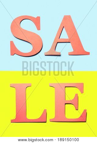 Vertical sale sign. Red orange letters cut from cardboard paper on light blue and yellow background. Colourful craft banner for marketing a special offer campaign. Vibrant summer design for business.