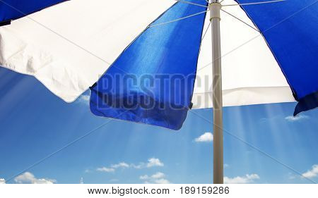 Striped beach umbrella against the sun against the blue sky and white clouds in the sun in the summer