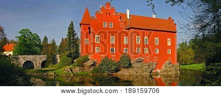 Panoramic view on traditional european antique red castle Cervena Lhota with bridge. Famous Czech Republic Renaissance castles. Red castle among green forest trees, at forest pond. Famous sightseeing