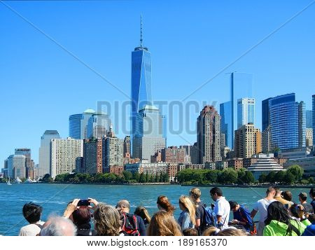 View on NYC New York Manhattan buildings skyscrapers from cruise sightseeing boat with photo shooting tourists. NYC skyscrapers architecture. Boat trip to Statue of Liberty. Famous sightseeing