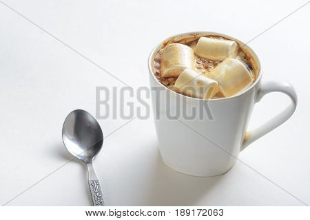 Cup Of Coffee with Marshmallows and a spoon on the table. White mug of hot drink with copy space background