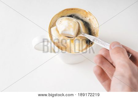 Mixing a spoon of coffee in a cup of marshmallows. White mug of hot drink with copy space background