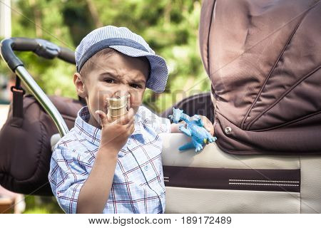 Big brother watching and guarding his junior brother in perambulator while walking in summer park and eating ice cream as concept for family ties