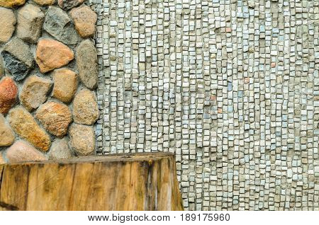 The junction of a cobblestone wall with wood and a shallow mosaic. Wall with various finishes with natural stoneand wood. Mixed finishing wall