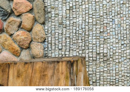 The junction of a cobblestone wall with wood and a shallow mosaic. Wall with various finishes with natural stoneand wood. Mixed finishing wall