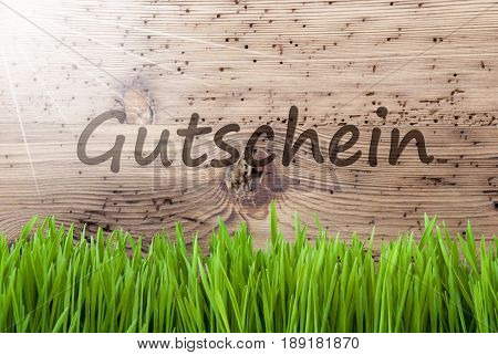 German Text Gutschein Mean Voucher. Spring Season Greeting Card. Bright, Sunny And Aged Wooden Background With Gras.