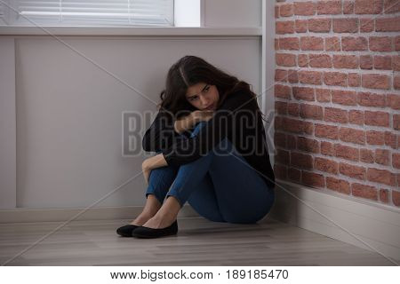 Sad Young Woman Sitting At The Corner Of The Room At Home
