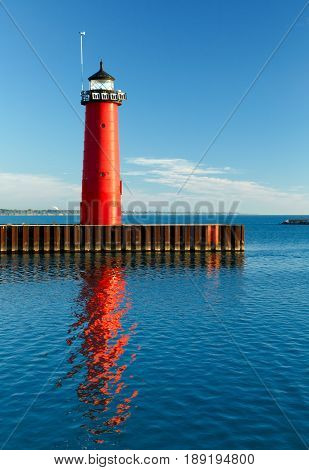 The bright red Pierhead Lighthouse at Kenosha Wisconsin is reflected in early morning light on the waters of Lake Michigan.