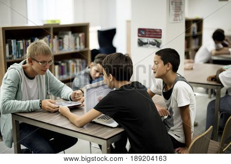 Group of diverse high school students using laptop in library
