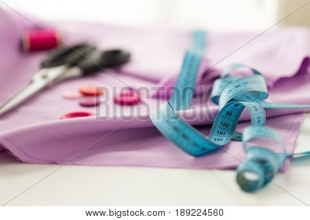 needlework and tailoring concept - scissors, sewing buttons, tape measure and cloth