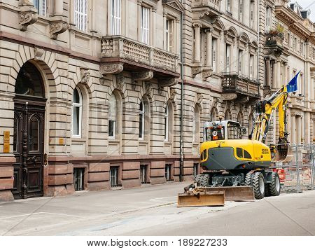 STRASBOURG FRANCE - MAY 18 2016: Wacker Neuson Yellow excavator working in urban environment with luxury apartment office historic building behind