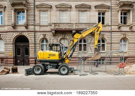 STRASBOURG FRANCE - MAY 18 2016: Wacker Neuson Yellow excavator working in urban environment with luxury apartment office historic building behind