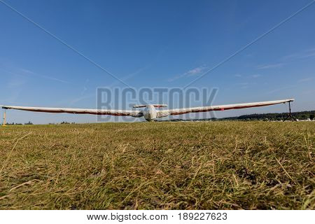 A glider with a protective sleeve parked on a grassy airport on a sunny day.