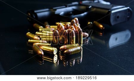 Black hand gun and bullets on the black mirror background.