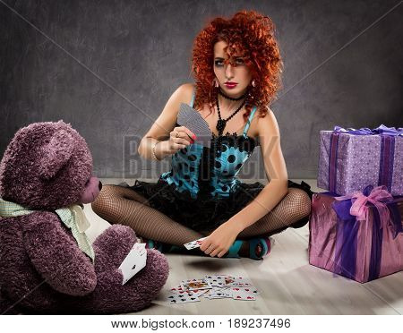 popsy play cards with a teddy bear. Curly redhead sexy girl looks like a doll for adult men. Beside gift boxes