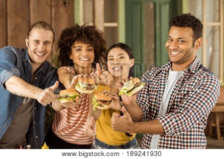 Young Smiling Multiethnic Friends Holding Burgers At Picnic On Patio