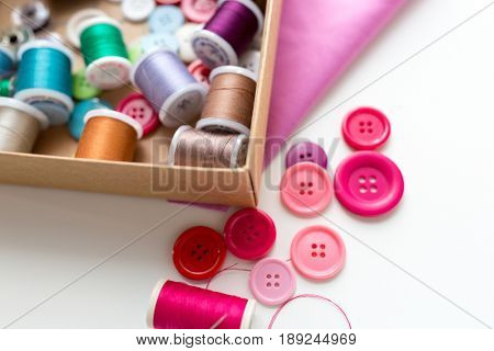 needlework, craft, sewing and tailoring concept - box with thread spools and buttons on table