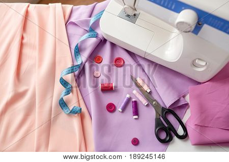needlework, technology and tailoring concept - sewing machine with scissors, buttons, tape measure and fabric