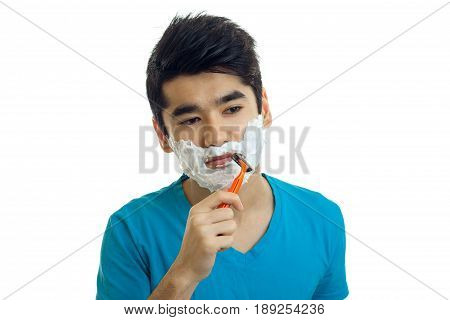 Portrait of a young guy with foam on his face that smiles and shaves his beard machine is isolated on a white background