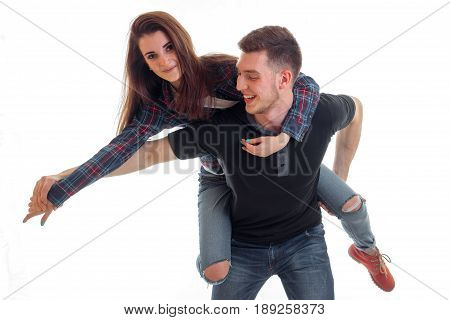 a cheerful young girl stands on the back of a young handsome guy and laughs is isolated on a white background