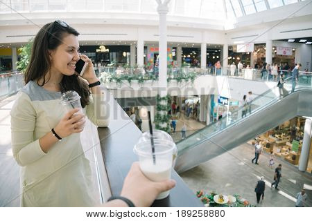 Young woman talking on the phone while walking mall with smoothie, firts-pesron view